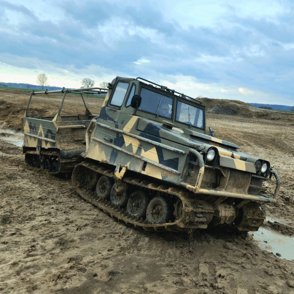 Na zdjęciu widać potężny pojazd gąsienicowy poruszający się po błotnistym terenie, przypominający atrakcje związane z monster truckami dla entuzjastów ekstremalnych przeżyć.
