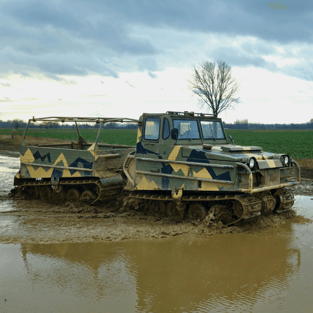 Pojazd terenowy o militarnej stylistyce, zanurzający się w błotnistej kałuży na tle polnej krajobrazu z bezlistnym drzewem.