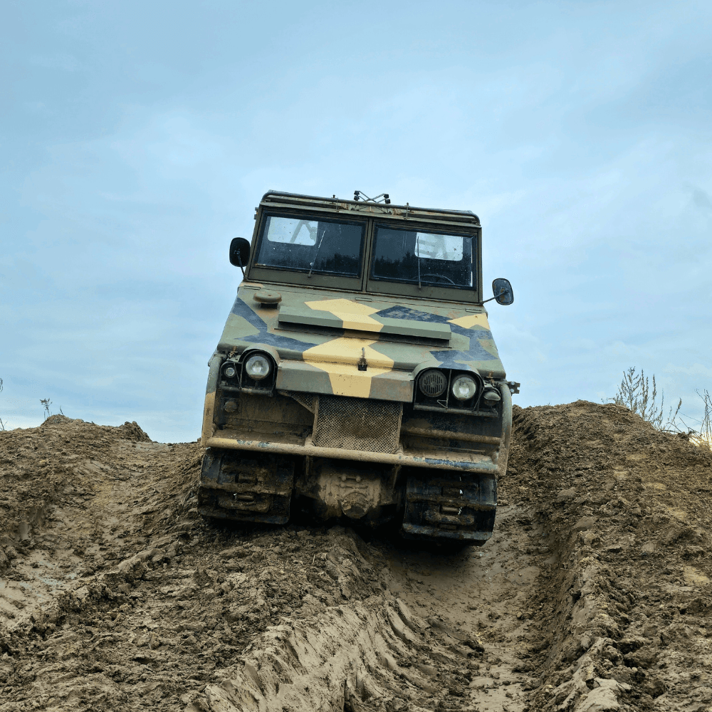 Na zdjęciu widać pojazd o wyglądzie wojskowym pokonujący błotnisty teren, co może być atrakcją dla miłośników monster trucków.