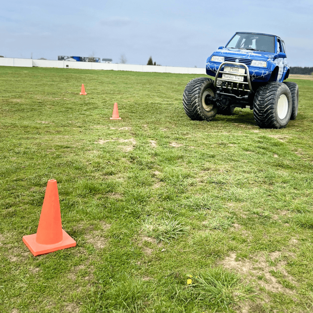 Niebieski monster truck stoi na trawiastym placu, otoczony pachołkami, gotowy do emocjonującej jazdy terenowej.