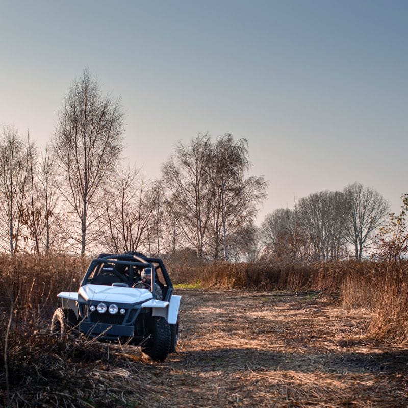 Na obrazie przedstawiono terenowy pojazd gotowy do off-roadowych szaleństw, przemierzający polną drogę pośród bezlistnych drzew.