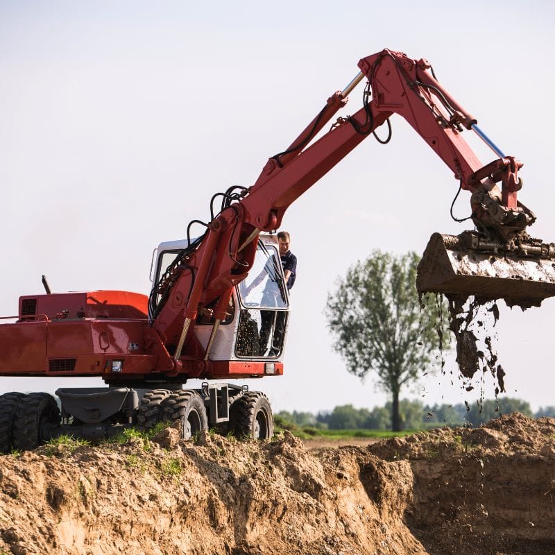 Na zdjęciu widać w akcji koparkę, której operator przenosi ziemię w otwartym terenie, symbolizującą dynamiczny świat ciężkich maszyn w Gassy pod Warszawą.
