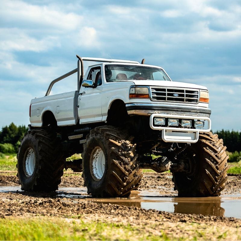 Potężny monster truck w białym kolorze przemierza błotnisty teren, oferując emocjonującą atrakcję w malowniczym otoczeniu niedaleko Warszawy.