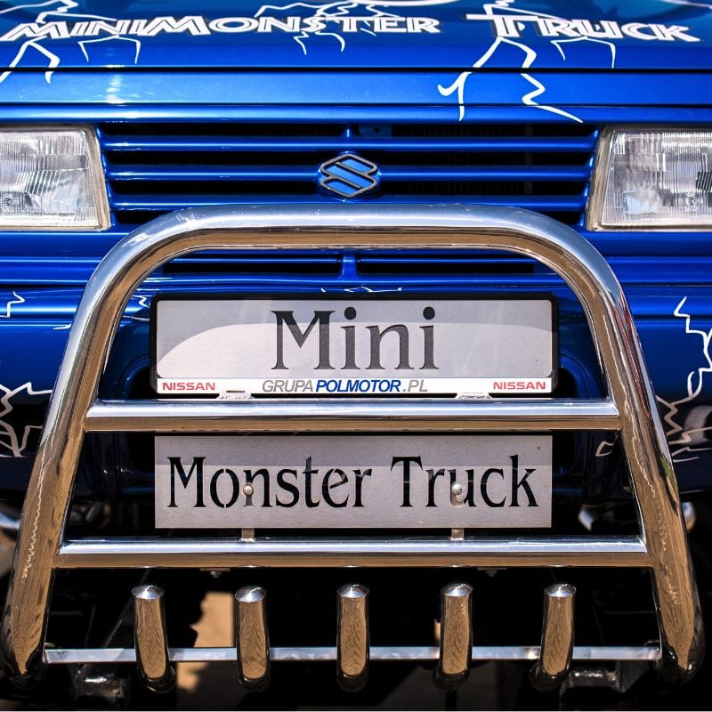 Na zdjęciu widoczny jest przód niebieskiego pojazdu z chromowanym zderzakiem i tabliczką Mini Monster Truck.