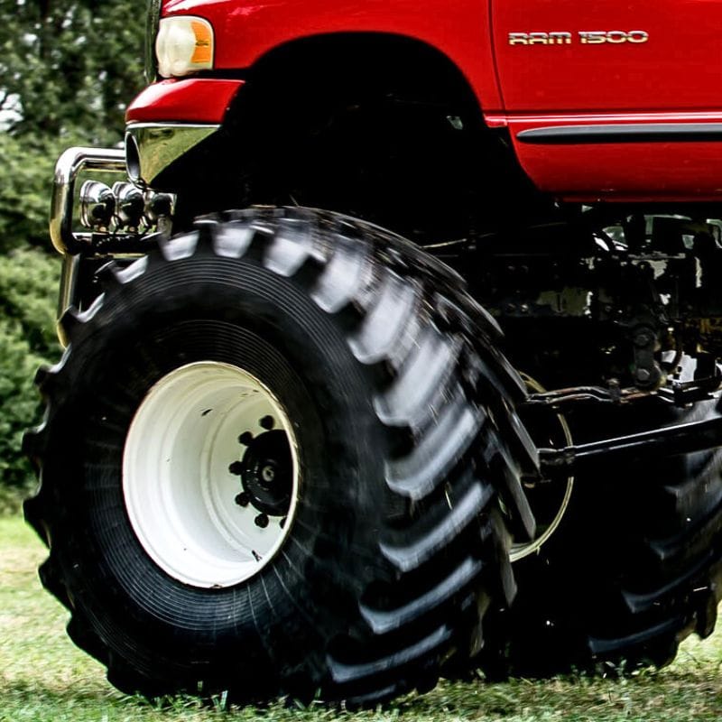 Czerwony monster truck z ogromnymi oponami stoi na trawie, ukazując potęgę i emocje, jakie można przeżyć w atrakcjach koło Warszawy.