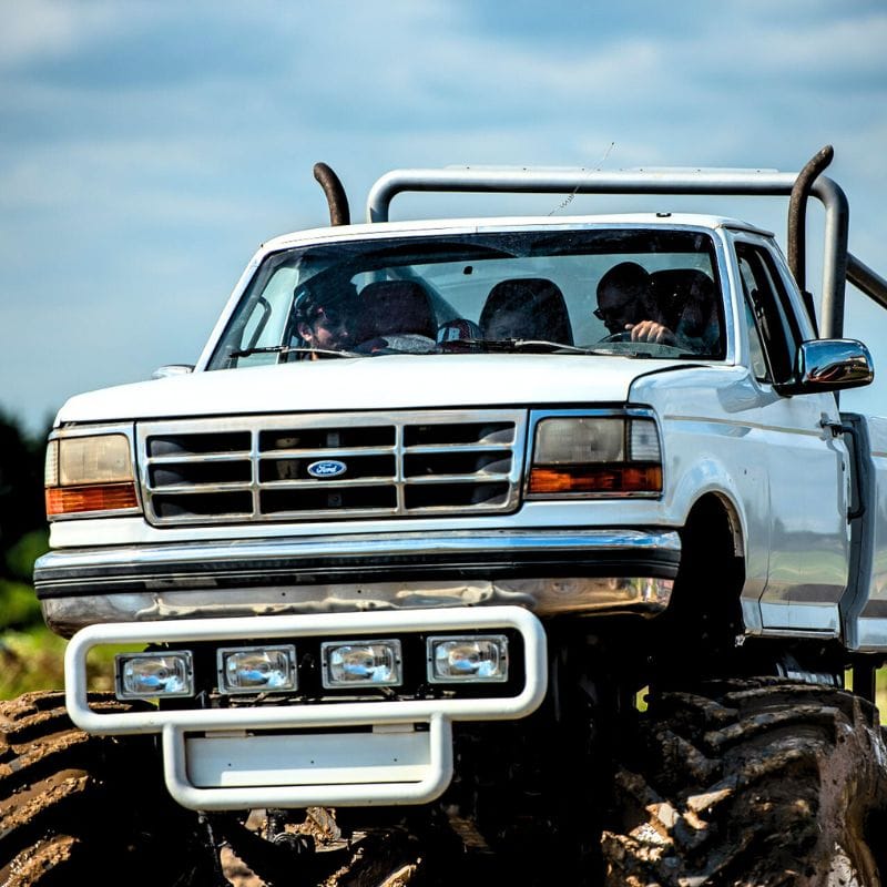 Zdjęcie przedstawia potężny biały monster truck w trakcie jazdy, wzbudzający emocje i przyciągający uwagę miłośników motoryzacyjnych atrakcji w okolicach Warszawy.
