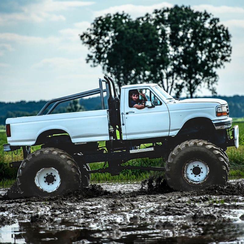 Na zdjęciu widać białego monster trucka przemierzającego błotnisty teren, co zapewnia ekscytującą atrakcję dla fanów motoryzacyjnych wrażeń.