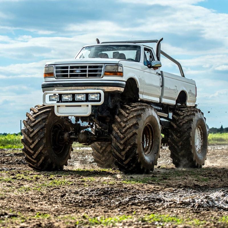 Ogromny monster truck sunie przez błotnisty teren, emanując siłą i przyciągając wzrok swoim masywnym podwoziem i wielkimi oponami.