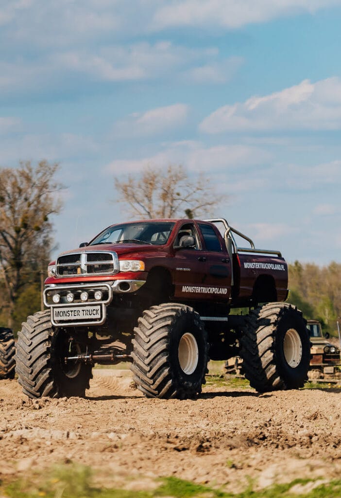 Potężny monster truck w akcji prezentuje swoje imponujące rozmiary na tle błękitnego nieba, podkreślając atrakcje dostępne w Gassy koło Warszawy.
