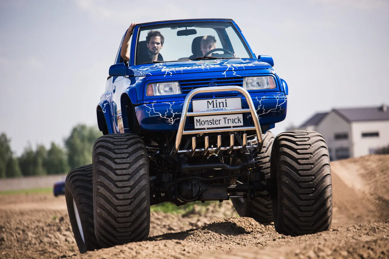 Niebieski Mini Monster Truck z kierowcą i pasażerem przemierza piaszczystą trasę, pokazując atrakcje off-roadowe w pobliżu Warszawy.