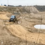 Na zdjęciu widzimy monster trucka pokonującego błotnisty tor off-road w surowym krajobrazie, zapewniając emocjonującą atrakcję dla fanów motoryzacyjnej przygody.