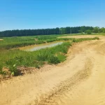 Na zdjęciu widać szeroki, piaszczysty tor terenowy otoczony zielenią, idealny do ekstremalnych przygód z monster truckami w malowniczej lokalizacji pod Warszawą.