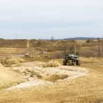Na rozległym, piaszczystym terenie widać monster trucka przemierzającego pagórkowaty krajobraz, idealny na emocjonujące atrakcje nieopodal Warszawy.