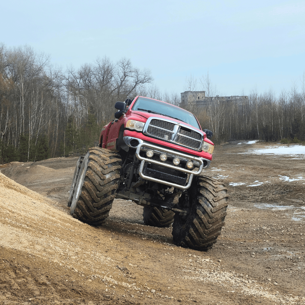 Gigantyczna ciężarówka typu monster truck w intensywnym czerwonym kolorze wspina się na nierówny teren, gotowa zapewnić emocje miłośnikom motoryzacyjnych atrakcji w każdym wieku.