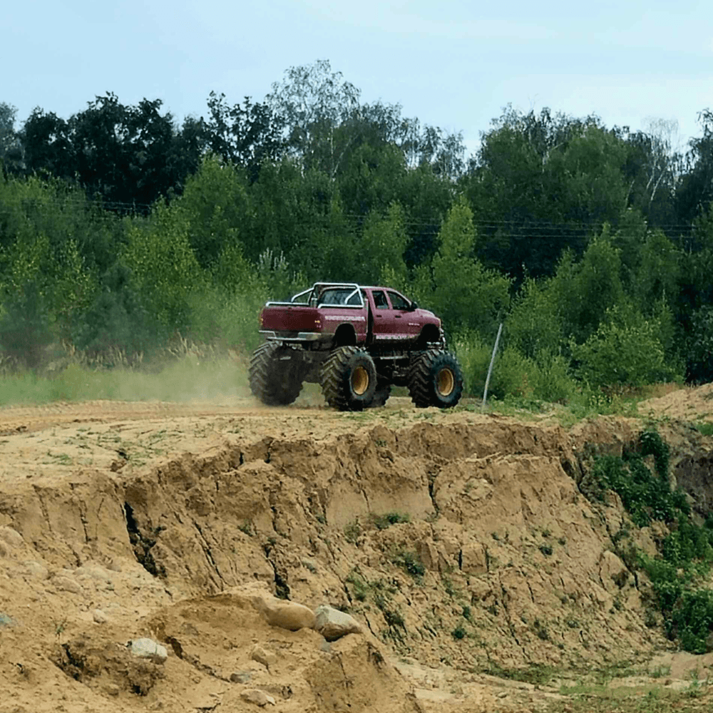 Potężny monster truck przemierzający piaszczysty teren w otoczeniu zieleni, zapewnia ekscytujące wrażenia w Gassy niedaleko Warszawy.