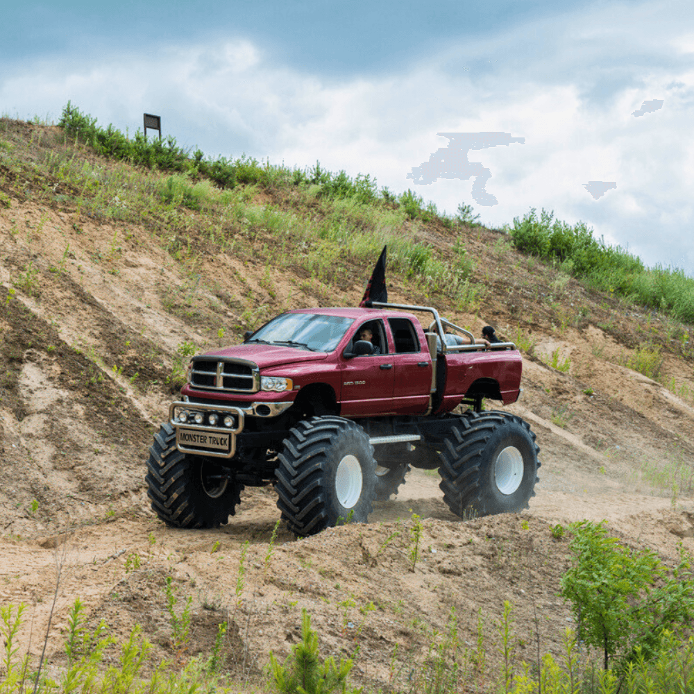 Czerwony monster truck z ogromnymi oponami wjeżdża na piaszczystą górę, oferując ekstremalne emocje dla miłośników motoryzacji w każdym wieku.