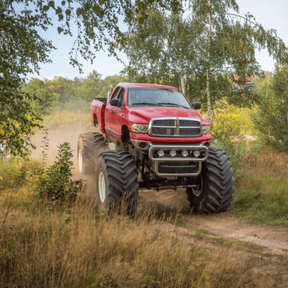 Czerwony monster truck przemierza leśną ścieżkę, pokazując swoje niezwykłe możliwości terenowe.