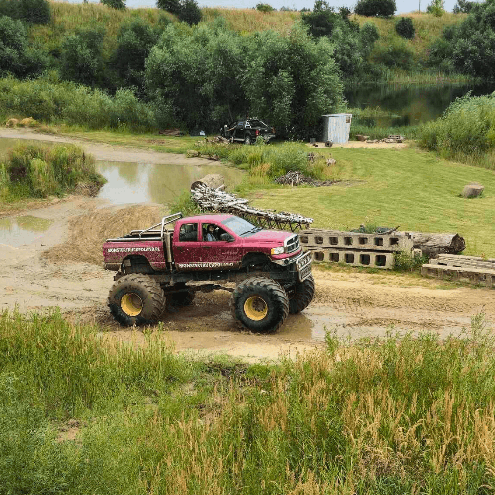 Na zdjęciu widać potężny monster truck, poruszający się po błotnistym terenie na tle zieleni, będący częścią atrakcji w Monster Truck Poland w Gassach pod Warszawą.