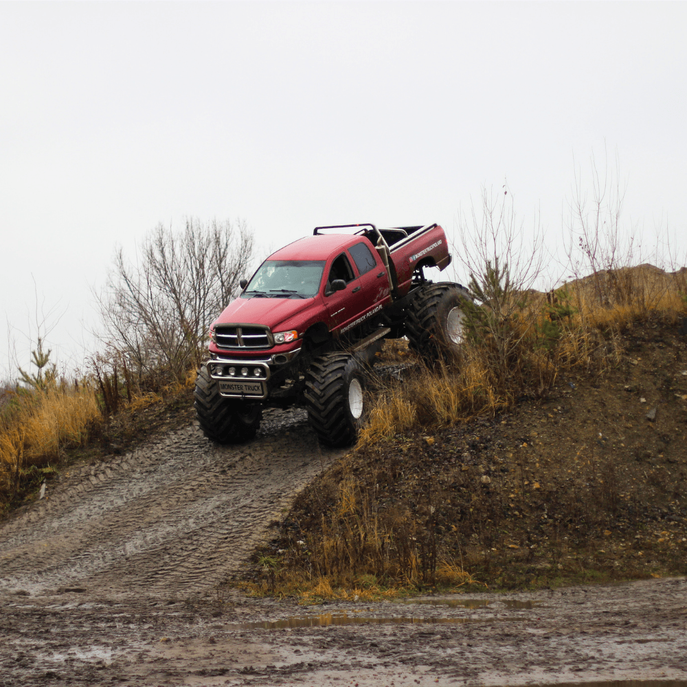 Na zdjęciu widać potężnego monster trucka pokonującego błotnistą, terenową trasę, co jest atrakcją dla miłośników adrenaliny w każdym wieku.