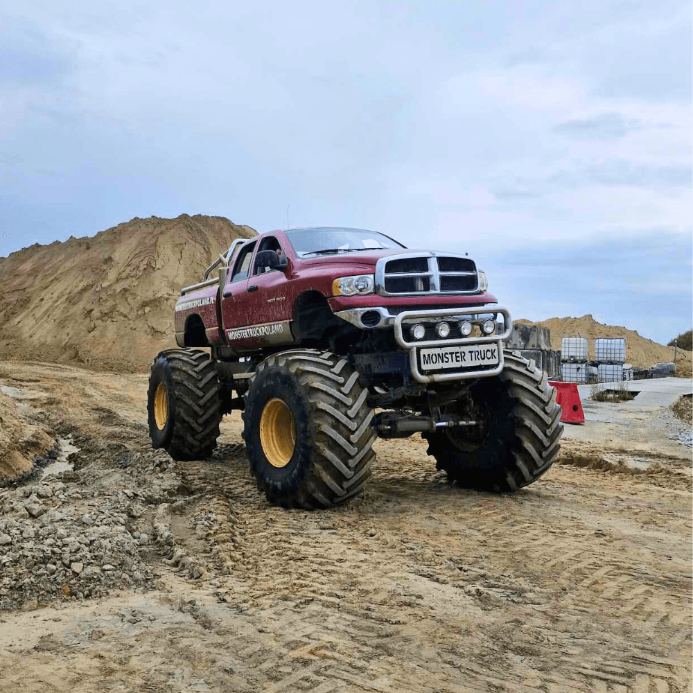 Ogromny monster truck stoi dumnie na piaszczystym terenie, reprezentując atrakcje dla fanów motoryzacyjnych emocji tuż obok Warszawy.