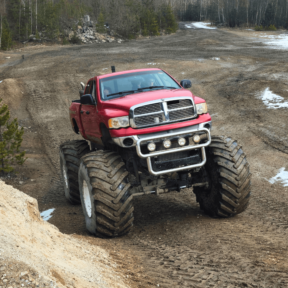 Na zdjęciu widać potężnego monster trucka z wielkimi oponami, który przemierza błotnisty teren, oferując niezapomniane emocje dla fanów motoryzacji.