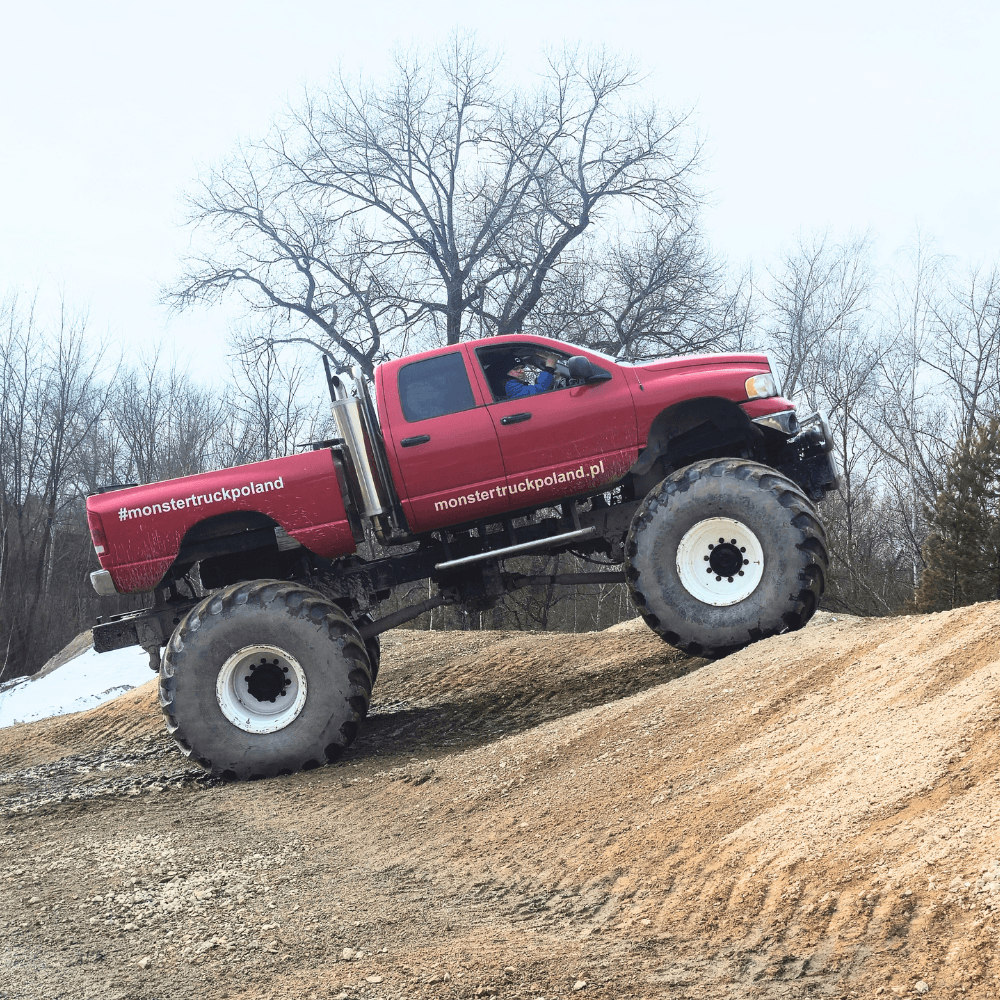 Ogromny, czerwony monster truck pokonuje stromą, piaszczystą górkę, oferując ekscytującą atrakcję pod Warszawą.