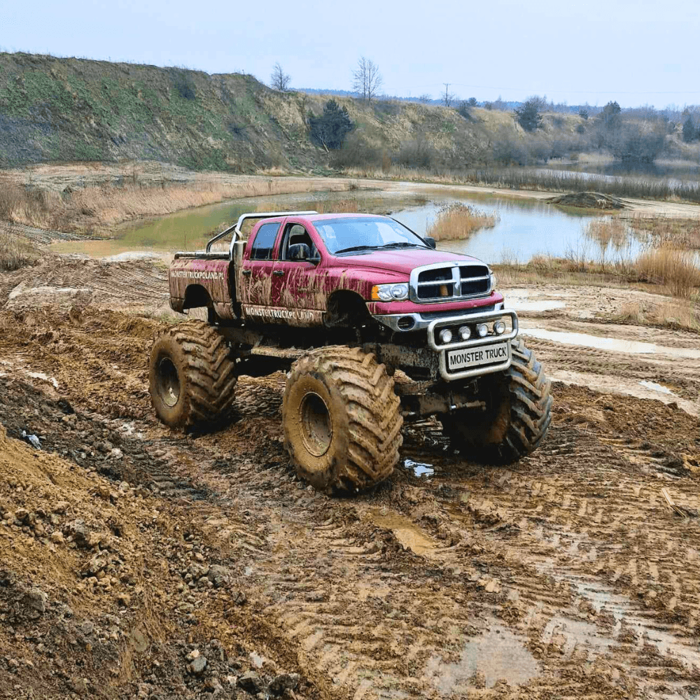Ogromny monster truck w terenie błotnistym oferuje emocjonującą atrakcję terenową na tle pięknego krajobrazu.
