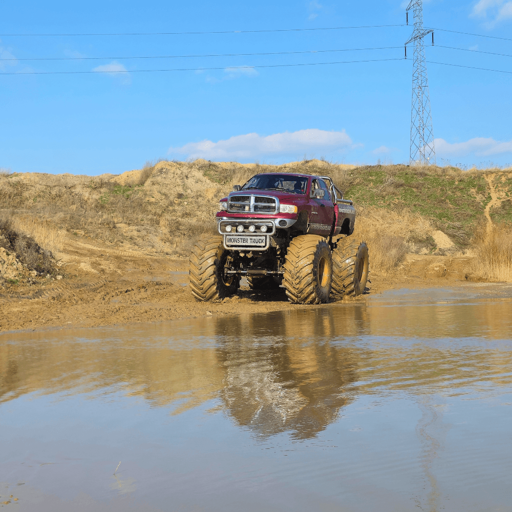 Na zdjęciu widać potężny monster truck pokonujący błotnistą trasę na tle malowniczego krajobrazu.